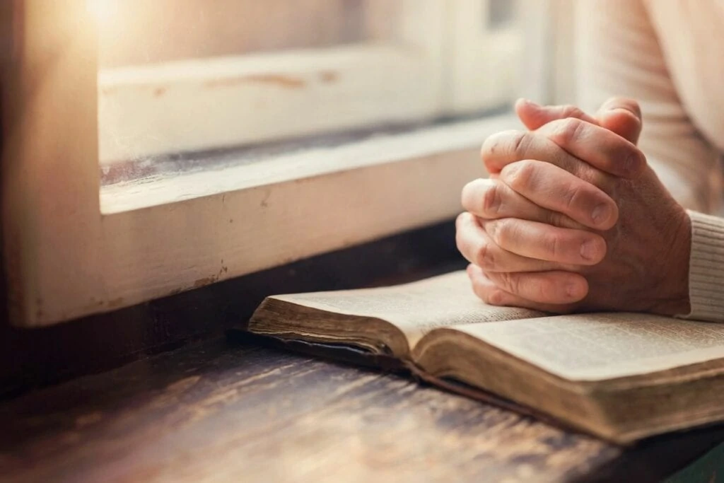 Hands folded over open bible.